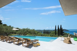 Ein Poolbereich mit Liegestühlen, einem Tisch und Blick auf das Meer und die Berge.
