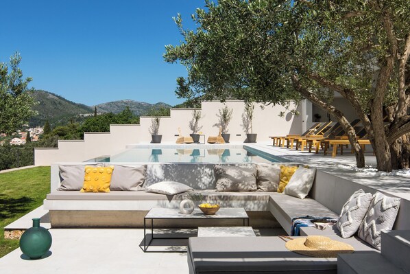 Ein zeitgemäßer Außenbereich mit Pool, einer Couch mit Kissen, einem Couchtisch und einer dekorativen Vase.