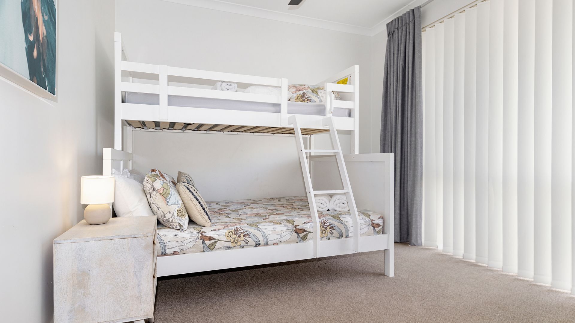 A bunk bed with a ladder, a bedside table with a lamp, and a floral-patterned mattress.