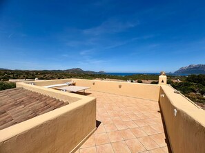 Eine Dachterrasse mit Blick auf Meer und Berge, ein Fliesenboden und ein kleiner Tisch mit einem Stuhl.