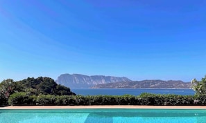 A pool with a view of a mountain range and the sea.