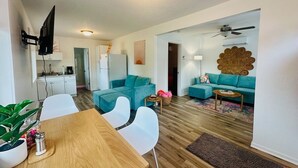 A modern living room with a wooden dining table, teal sofas, and a kitchen area in the background. - Terrific lake view! On the shoreline. (Sunrise Beach)