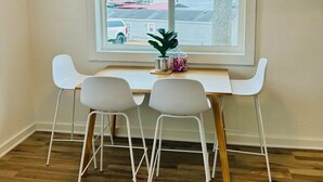 A room with a white table and four white chairs, a window with blinds, and a view of a body of water and a red vehicle outside. - Terrific lake view! On the shoreline. (Sunrise Beach)