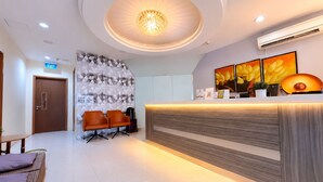 A hotel reception area with a modern design, including a reception desk, seating area, and a decorative wall. - Amrise Hotel Geylang (Singapore)