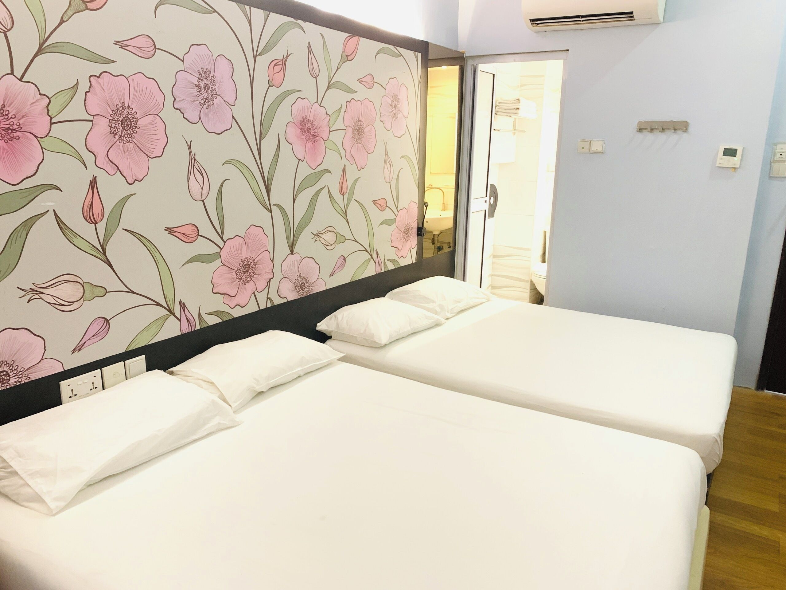 A hotel room with two beds, a floral wallpaper, and a bathroom visible through an open door.