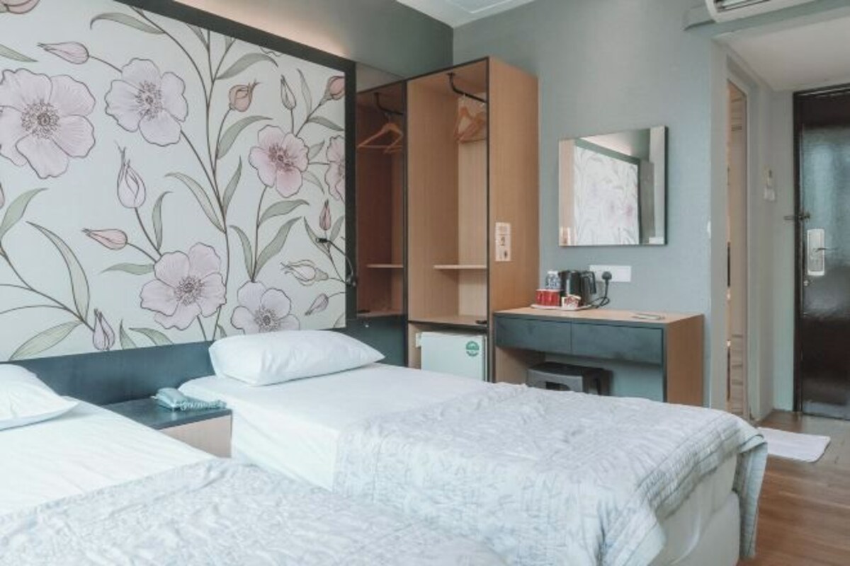 Habitación de hotel con dos camas, un armario, un escritorio con espejo y un diseño floral en la pared.