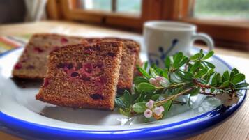 A slice of cake with berries on a plate, a cup, and some greenery.