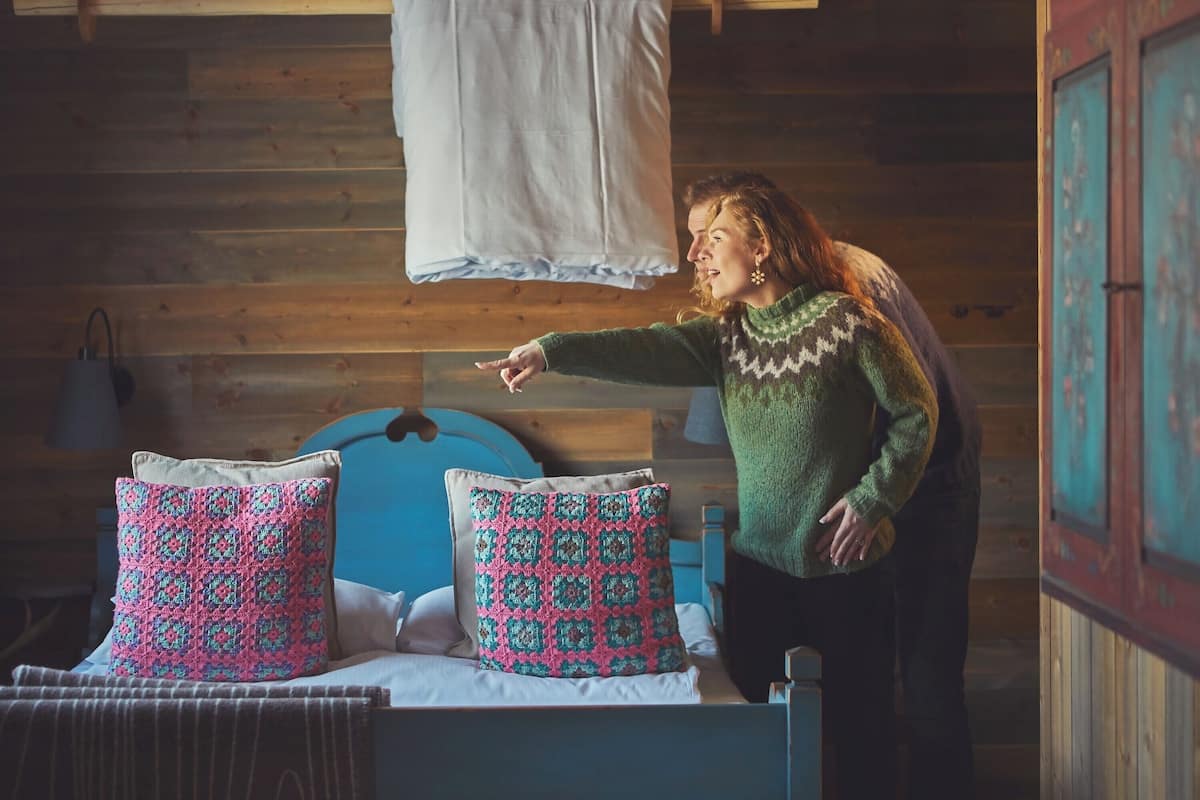 A wooden cabin interior with a bed, pillows, and a hanging white cloth.