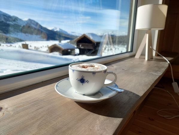 Una taza de café sobre un plato junto a una ventana con vista a una montaña nevada.