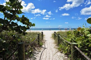A sandy beach path leading to the ocean, surrounded by greenery and wooden posts. - Charming 2 bedroom & office-minutes from the Beach- freshly renovated with pool! (Nokomis)