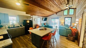 A modern kitchen with wooden beams, a central island with stools, and a dining area with a sofa and table. - Astonishing view 100 feet from the lake! (Sunrise Beach)