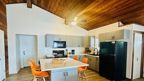A modern kitchen with wooden ceiling beams, a central island with orange chairs, and a black refrigerator. - Astonishing view 100 feet from the lake! (Sunrise Beach)