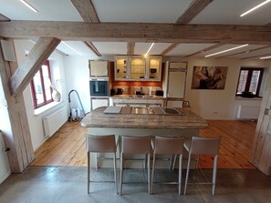 Une cuisine moderne avec des poutres en bois, un îlot central doté de tabourets et des appareils électroménagers intégrés.