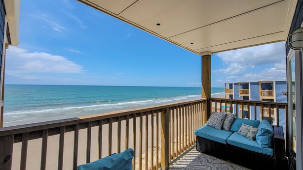 A beach view from a covered balcony with a wicker sofa and cushions. - Topsail Reef 358: Dream2B - Oceanfront Getaway! (North Topsail Beach)