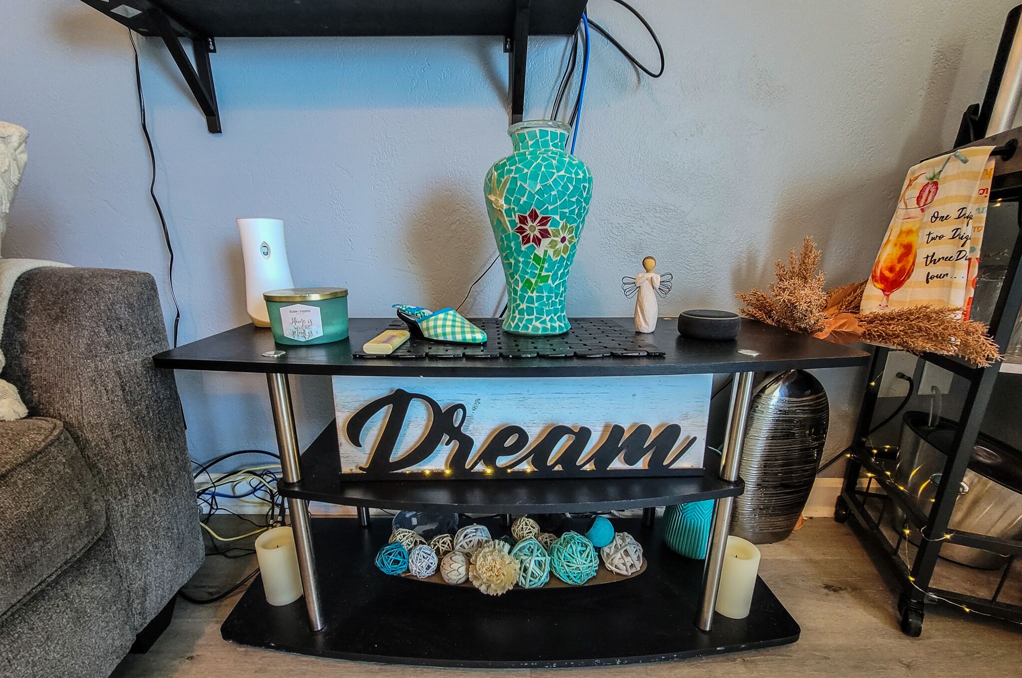 A black shelf with a 'Dream' sign, a teal mosaic vase, a candle, a small figurine, and decorative items.