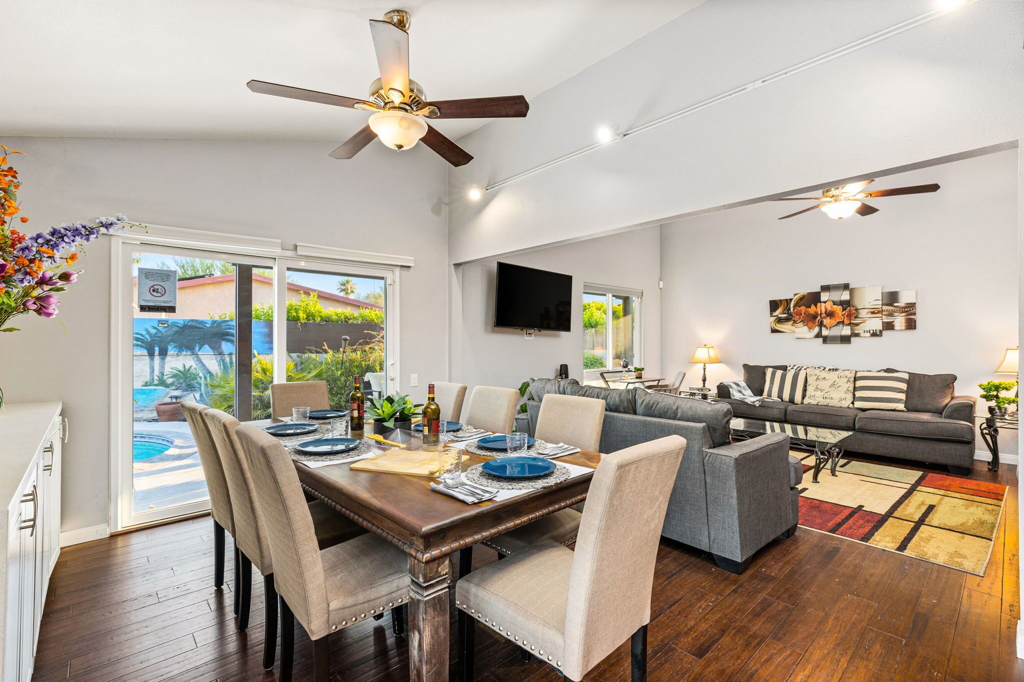 A modern living room with a dining area, a grey sofa, a flat-screen TV, and a ceiling fan.
