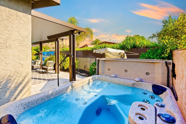A hot tub with a stone exterior, surrounded by a patio area with chairs and a covered seating area.