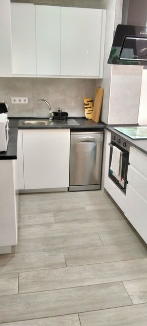 A modern kitchen with white cabinets, a stainless steel dishwasher, a built-in oven, and a black microwave.