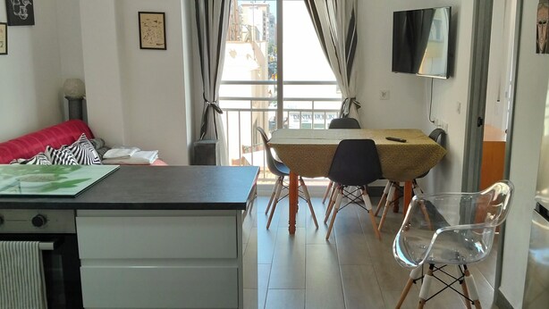 A compact kitchen with a dining area, a TV mounted on the wall, and a view of the city through the window.