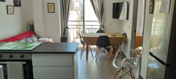 A compact kitchen with a dining area, a TV mounted on the wall, and a view of the city through the window.
