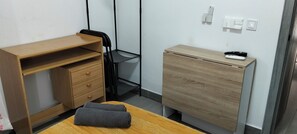 A compact room with a wooden desk, a chair, a small cabinet, and a table with a towel.