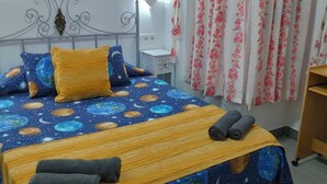 A bedroom with a bed featuring a space-themed bedspread, a bedside table, a wooden desk, and a curtain with a floral pattern.