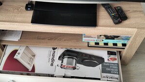 A wooden desk with a laptop, remote controls, and a box of Monopoly and Viaja.