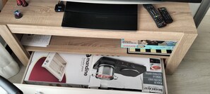 A wooden desk with a laptop, remote controls, and a box of Monopoly and Viaja.