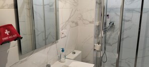 A bathroom with a marble floor, a glass shower enclosure, a sink with a mirror, and a red first aid kit.