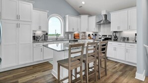 Una cocina moderna con armarios blancos, una isla grande con taburetes de bar, una estufa integrada y vistas a través de una ventana.