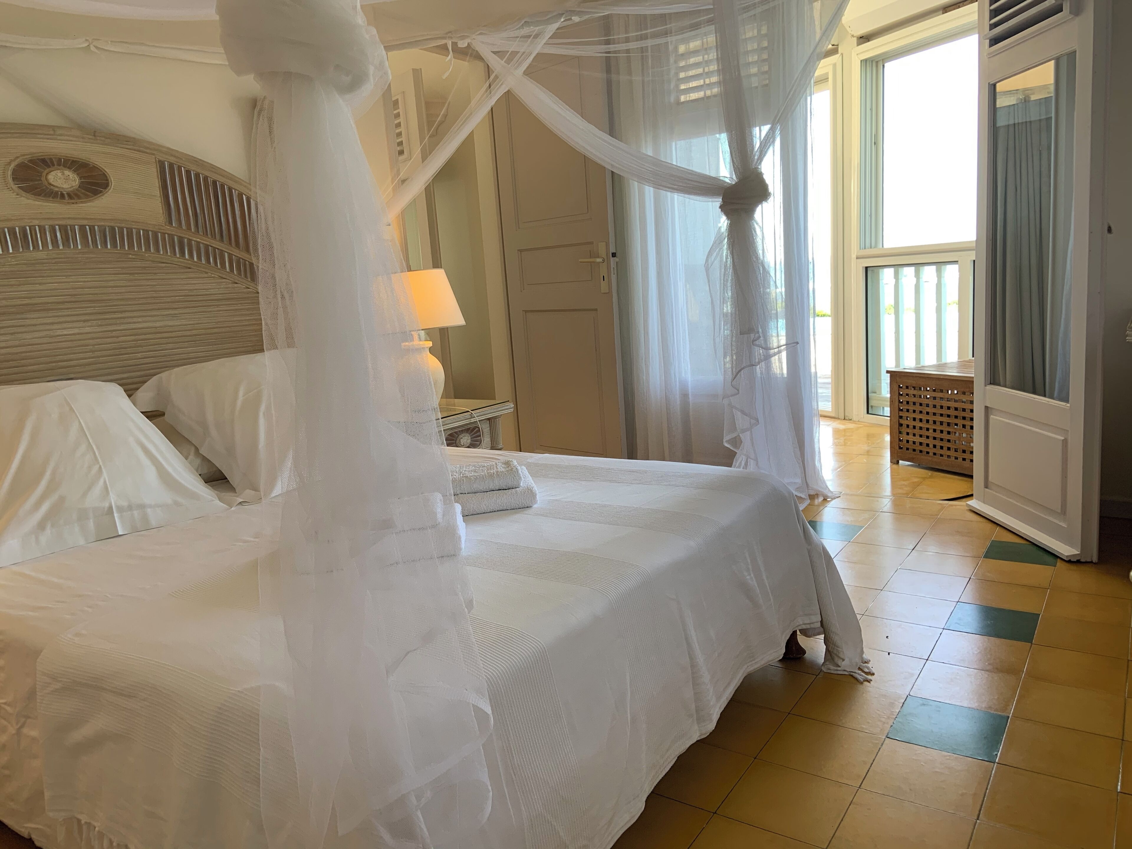 Un letto a baldacchino, un comodino con una lampada e vista all'esterno attraverso una porta.