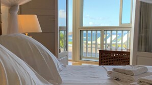 A hotel room with a bed, a view of the sea, and a balcony with a wooden table and chairs.