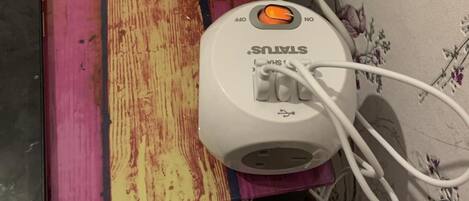 A white power strip with multiple white cables plugged in, placed on a wooden surface with a floral wallpaper background.