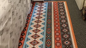 A room with a patterned carpet, a bed with a white sheet, and a grey carpeted floor.