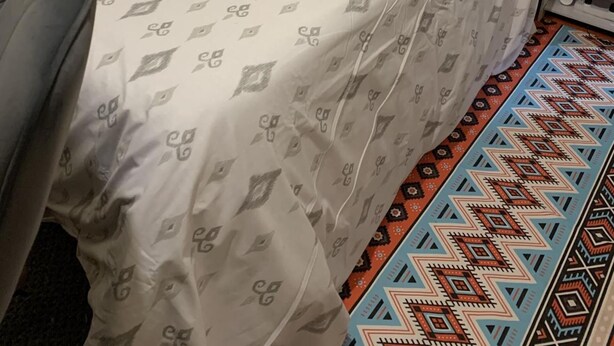 A bed with a patterned bedspread and a colorful geometric rug on the floor.