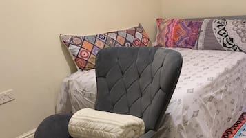 Quarto com uma poltrona estofada cinza, um edredom estampado e uma manta branca na cadeira.