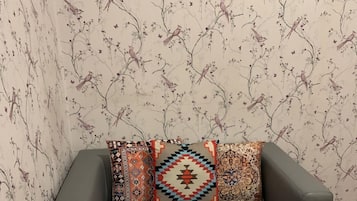 Um sofá cinzento com três almofadas estampadas em frente a um papel de parede floral.