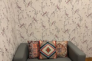 Un sofá gris con tres cojines estampados sobre un fondo de papel tapiz floral.