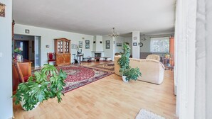 Tilava olohuone, jossa on suuri puulattia, punainen ja beigenvärinen matto, beigenvärinen sohva, puinen kaappi ja ruukussa oleva kasvi.