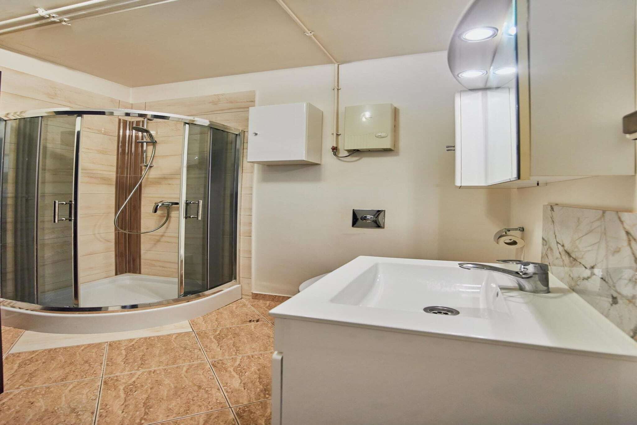 A modern bathroom with a glass-enclosed shower, a white sink, and a marble-tiled floor.