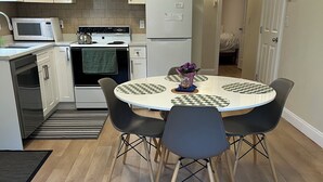 Ett modernt kök med vita skåp, en köksö med stolar, ett kylskåp och en mikrovågsugn.