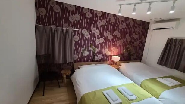 Una habitación de hotel con dos camas, una mesita de noche con lámpara, una pequeña mesa y una silla.