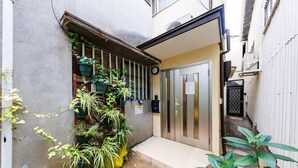 A narrow alleyway with a door leading to a building. There are potted plants along the wall and a small step leading to the entrance. - Sky Building Umeda (Osaka)