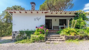 A small, single-story building with a stone chimney, a white exterior, and a porch with steps leading to the entrance. - Charming Home in a Green Valley. El Pigot. Tranquility, Nature & Private Pool! (Riudarenes)