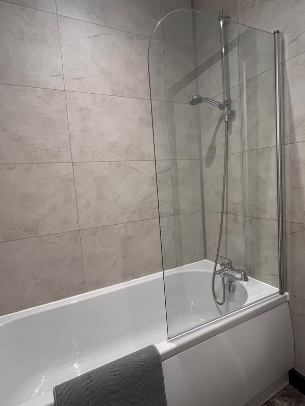 A modern bathroom with a glass-enclosed shower, a white bathtub, and tiled walls.