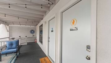 Un corridoio d'albergo con un tappetino di benvenuto, una sedia blu, una porta bianca con un cartello di avvertimento e luci a stringa sul soffitto.