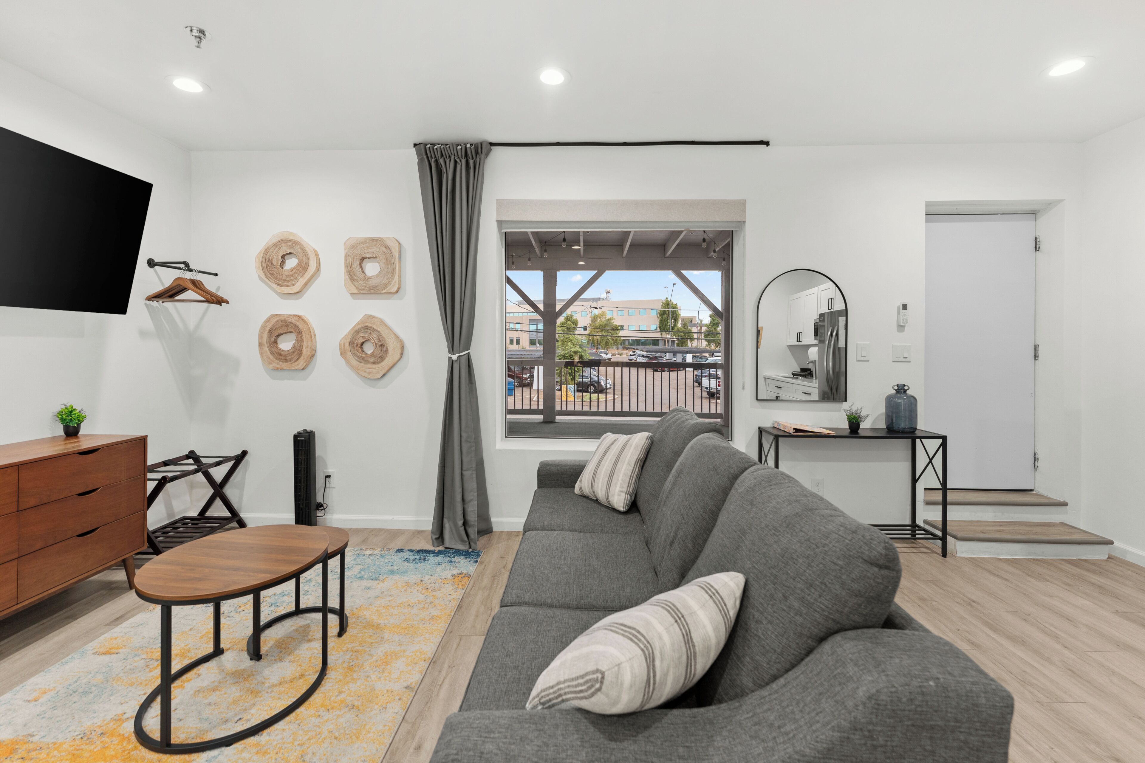 A modern living room with a grey sofa, wooden side table, and a flat-screen TV mounted on the wall.