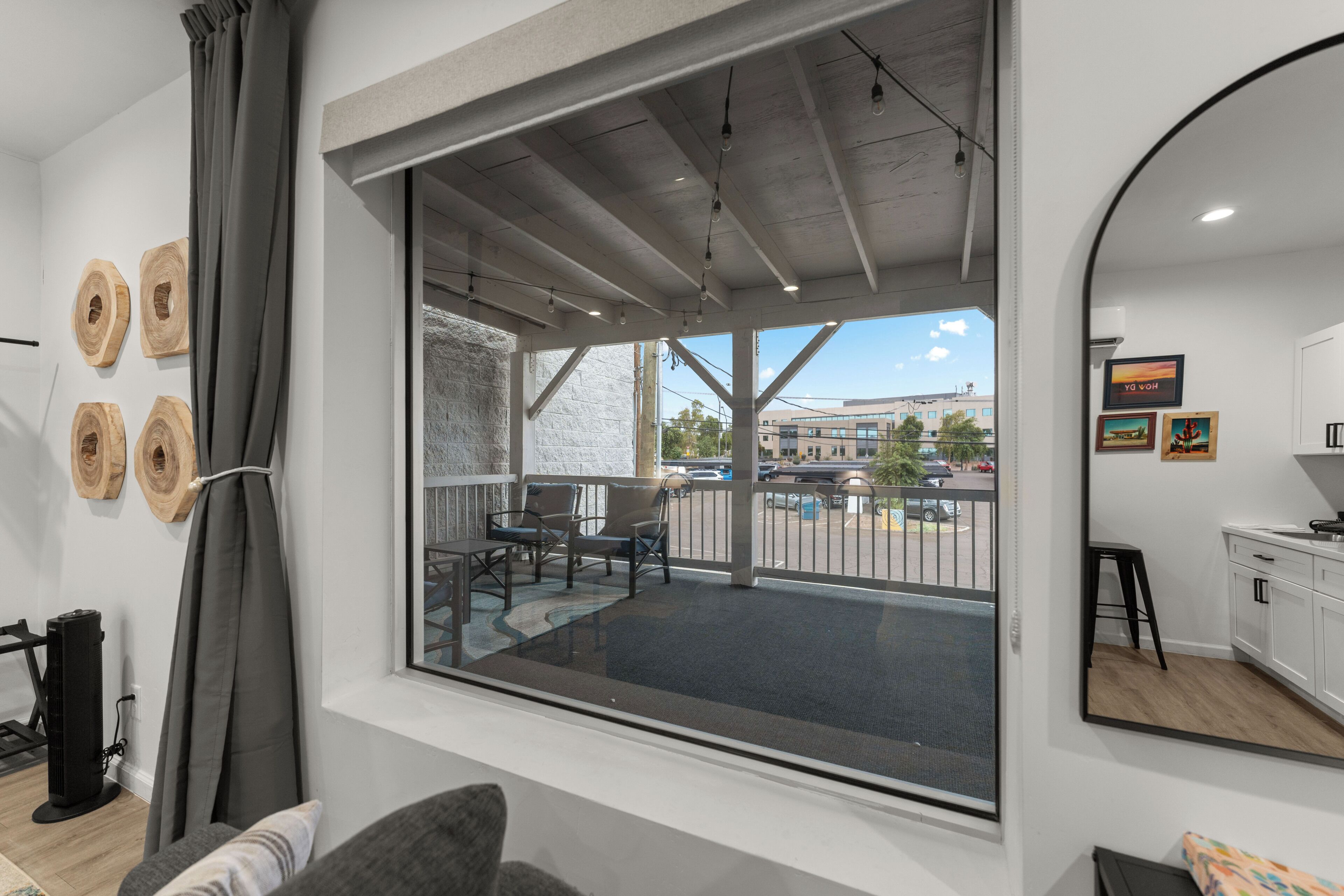 Une chambre d’hôtel moderne dotée d’une grande fenêtre, d’un balcon avec coin salon extérieur et d’une vue sur le paysage urbain.