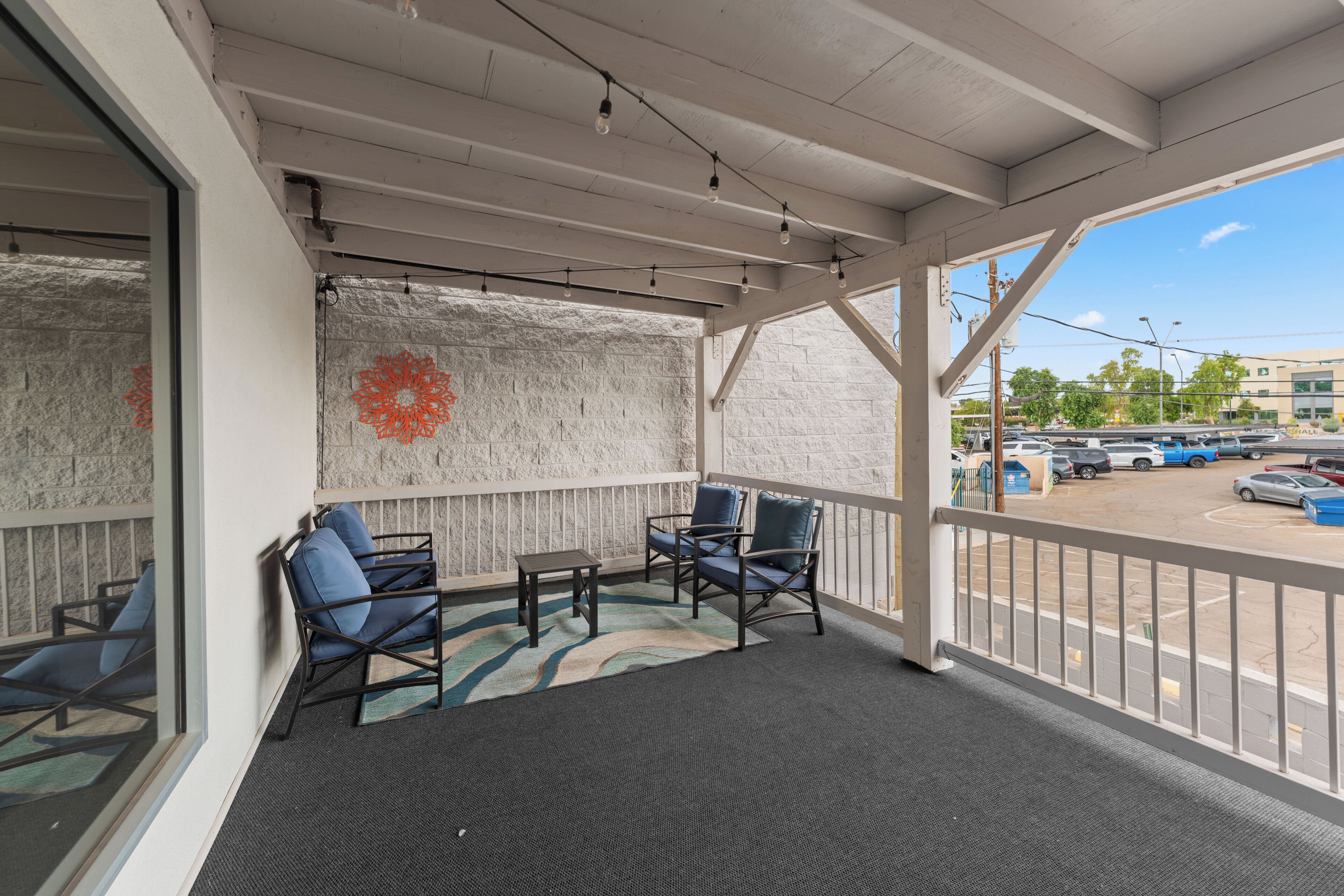 Un área de estar al aire libre cubierta con sillas y una mesa, un muro decorativo y vista a un estacionamiento.