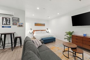 A modern hotel room with a bed, a sofa, a desk, and a TV.